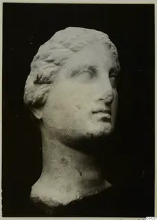 Marble head of a figure with wavy hair combed back, shown in three-quarter view against a black background.