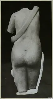 Back view of a headless marble statue with a broad diagonal band across the back, against a dark background