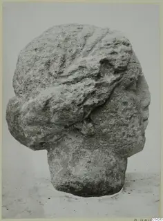 Stone head from Soli shown in right profile, with wavy hair swept back and a weathered, pitted surface.