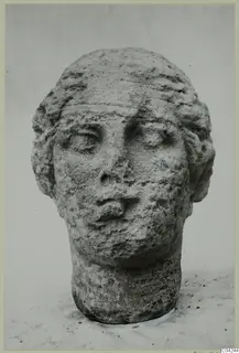 Stone female head with a broad face and hair framing it, photographed against a plain background
