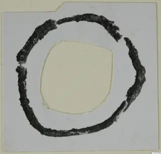 Dark ring-shaped bronze adornment on a mounted card, from Milia