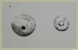 Two small perforated beads, one larger than the other, photographed on a plain grey background.