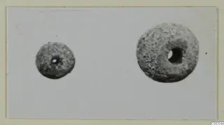 Two small rounded objects with central holes, one smaller than the other, photographed on a pale card.
