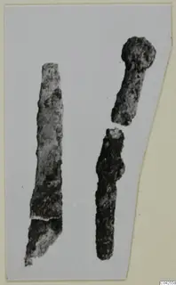 Two corroded bronze toilet requisites: a long flat blade and a knobbed rod, on a pale background.