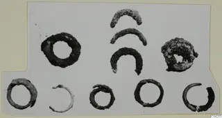 Bronze personal adornments from Milia: ten corroded metal rings and curved fragments laid out on a white card