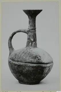 Base-ring style jug with a single loop handle and a flaring trefoil-like rim on a tall neck, photographed against a plain background.