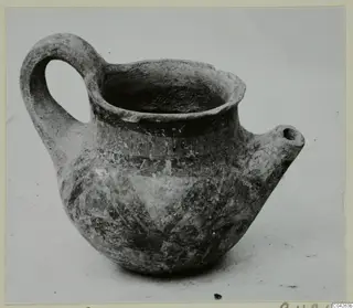 Pottery jug with a looped handle, a spout and painted bands, photographed on a plain surface.