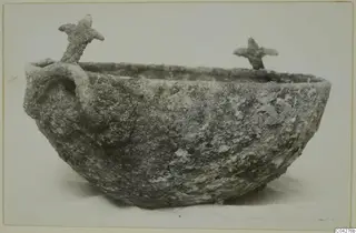 Corroded, encrusted bowl with a loop handle on one side and two upright projections on the rim