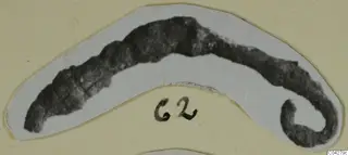 Dark, corroded curved bronze adornment with a coiled end, mounted on a card, from Amathus tombs.