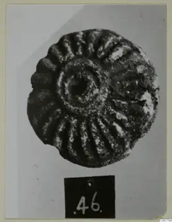 Round, corroded disc-shaped object with radiating ridges and a central hole, from Amathus