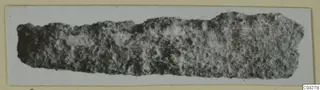 Corroded iron tool fragment from Amathus tombs, shown as a long, pitted strip on a card mount