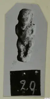 Small worn figurine of a standing figure from Amathus, photographed on grey card with a number label below.