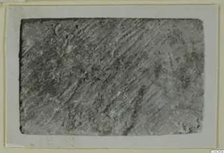 Close view of a grey rectangular bone fragment from Amathus, its surface marked with fine diagonal striations.