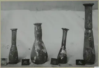 Four blown glass bottles of varying height, numbered 12 to 15, standing in a row on a pale cloth.