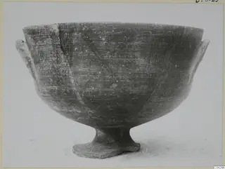 Footed bowl with two small side handles and scratched hatched decoration, shown on a pale surface