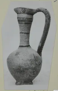 Painted pottery jug with a tall neck, a strap handle and dark horizontal bands, photographed on a light background.