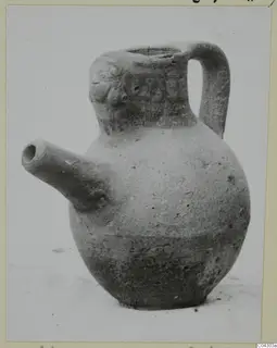 Pottery jug with a side spout, a strap handle and modelled face-like features on the neck
