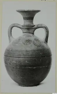 Round-bodied jug with flaring neck, two loop handles, dark painted bands and concentric circles, photographed against a plain background.