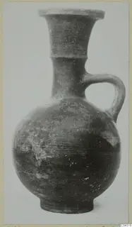 Pottery jug with a flared neck and a single strap handle, shown from the side against a pale background.