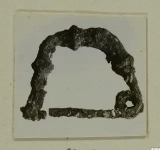 Corroded bronze object shaped like an arch, with a small loop at its right end, from Amathus