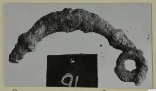 Corroded bronze object, curved like an arc with a ring at one end, from Amathus tombs 2-26.