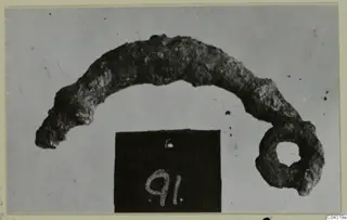 Corroded bronze object, curved like an arc with a ring at one end, from Amathus