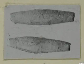 Two elongated bronze objects from Amathus, tapering at both ends, photographed on grey card