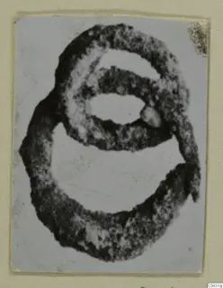 Jewellery from Amathus: a dark ring-shaped object of two overlapping loops, with a small knob, on a card mount.