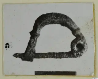 Iron tool from Amathus: an arched loop with a straight arm ending in a pointed tip, photographed on a card.