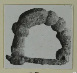 Corroded object from Amathus tombs 2-26, shown as an open, arch-shaped frame with a straight bar along the base.