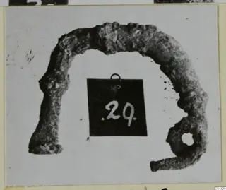 Corroded bronze arc-shaped object with a round hole at one end, from Amathus tomb 2-26