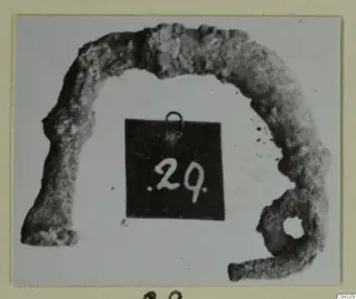 Corroded bronze part with a loop, photographed with a number label, from Amathus