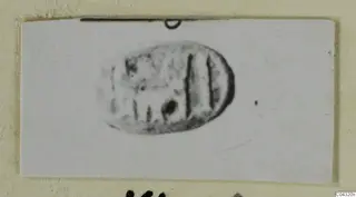 Engraved oval seal or gem with vertical incised lines and a round dot, photographed on a card mount