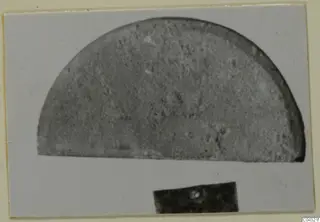 Half-round stone object, photographed on a light card, with a dark number label below