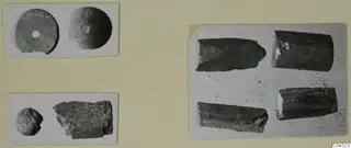 Photo mount showing small find objects: two discs, a rounded object, a rough fragment, and four dark cylindrical pieces.