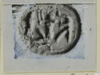 Glyptic: a rounded seal or gem with incised lines, shown in a damaged photograph on a grey card mount
