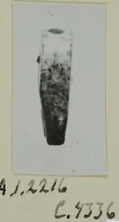 Small glyptic object, tapering with dark mottling and a dark oval at the top, shown on a card mount.