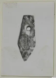 Flat pointed stone object with a drilled hole near its upper end, photographed against a pale background