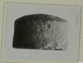 Blurred photograph of a dark stone object with a rounded top, mounted on a cream card