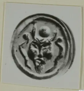 Round seal or gem in a circular frame, with a raised central motif of a face-like shape and a round element above it