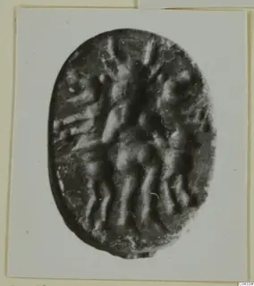 Oval dark stone seal or gem with a carved design, shown on a white card