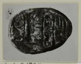 Oval seal-gem in dark stone with an incised design, shown on a card mount