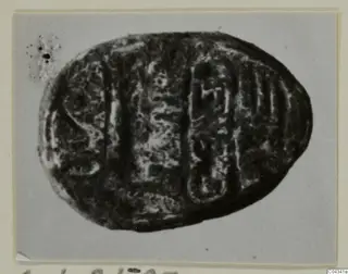 Oval dark stone seal with incised signs on its flat base, photographed on a grey card mount