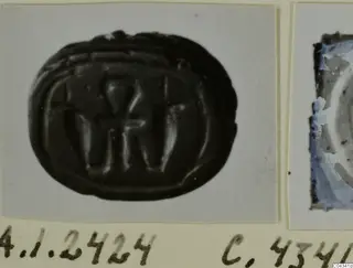 Dark oval stone seal with carved signs, photographed on a card mount, from Ayia Irini