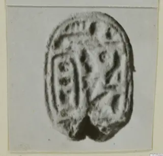 Oval stone seal with incised signs on its flat face, shown on a pale card mount