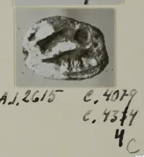 Oval seal or gem from Ayia Irini, dark and worn, with pale encrusted patches and two incised grooves