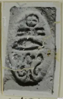 Enlarged photograph of an engraved seal or gem, with a small circle above horizontal bands and a curled motif below.
