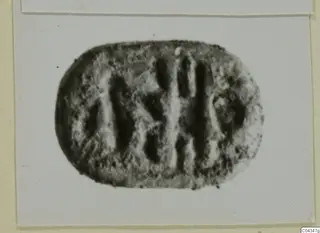 Oval stone seal with incised vertical strokes and marks, shown in a photograph on a card.