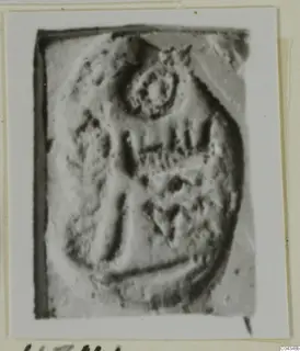Close view of an engraved stone seal or gem with a ring-shaped motif and vertical strokes, shown on a mounted card