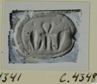 Oval seal or gem with an incised design of vertical strokes and a V-shaped mark, photographed on a card mount